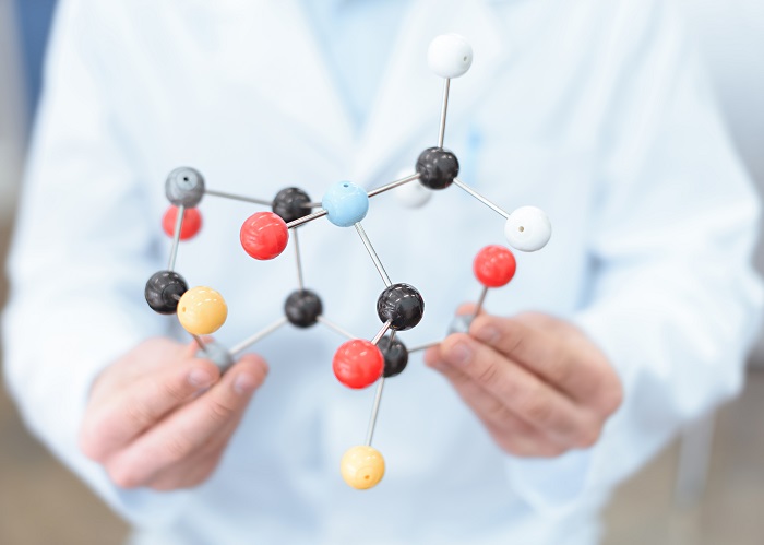 Close-up partial view of scientist in white coat holding molecular model